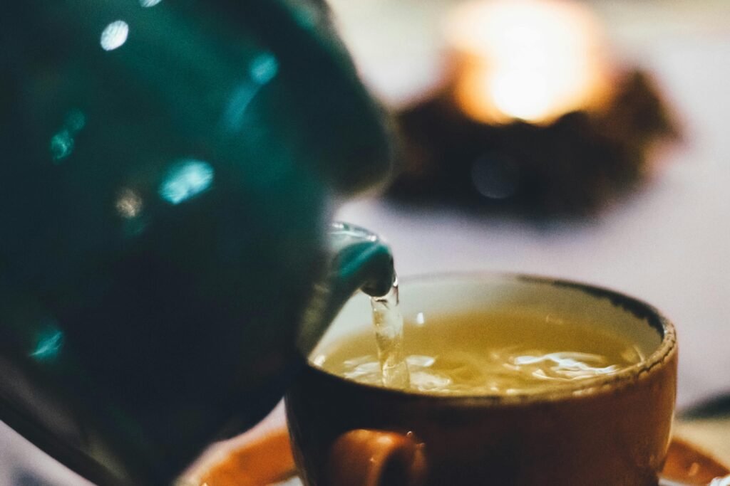 Warm close-up image of tea being poured into a teacup with blurred background ambiance.