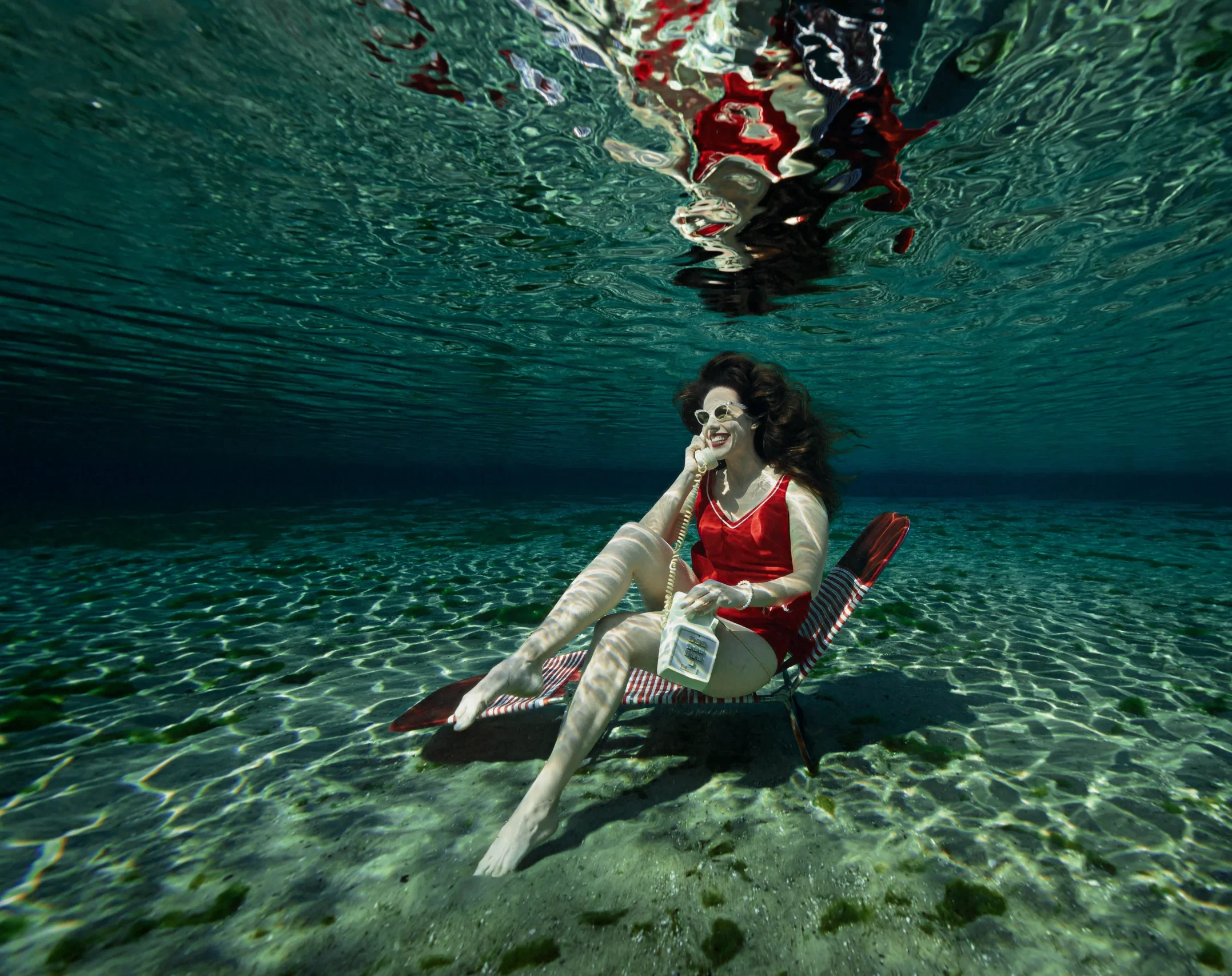 Underwater Model for Hire Shannon Scott talking on a telephone underwater while wearing a red swimsuit.