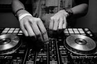 Voiceover 3 Close-up of a DJ's hands adjusting controls on a mixer in monochrome.