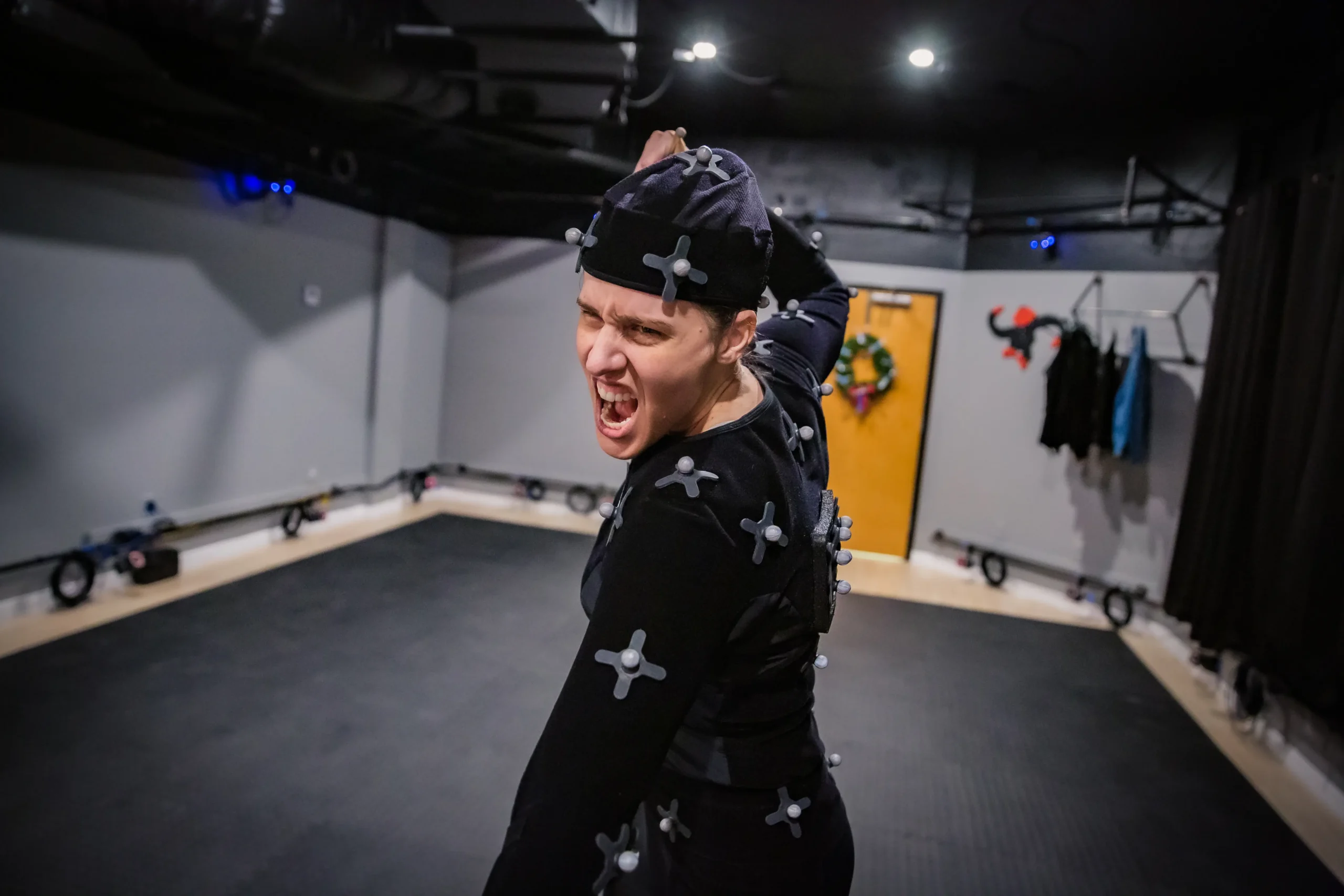 A performance capture actor wearing a motion capture suit screams dramatically inside a capture volume surrounded by tracking cameras.