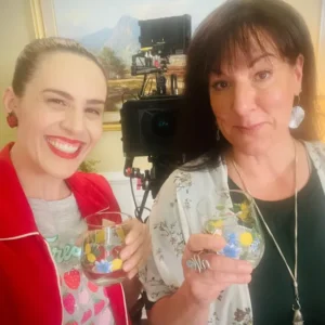 Shannon Scott and Toni Deckers cheer with glasses of water on set, celebrating collaboration, creativity, and building sustainable, creative income for actors.