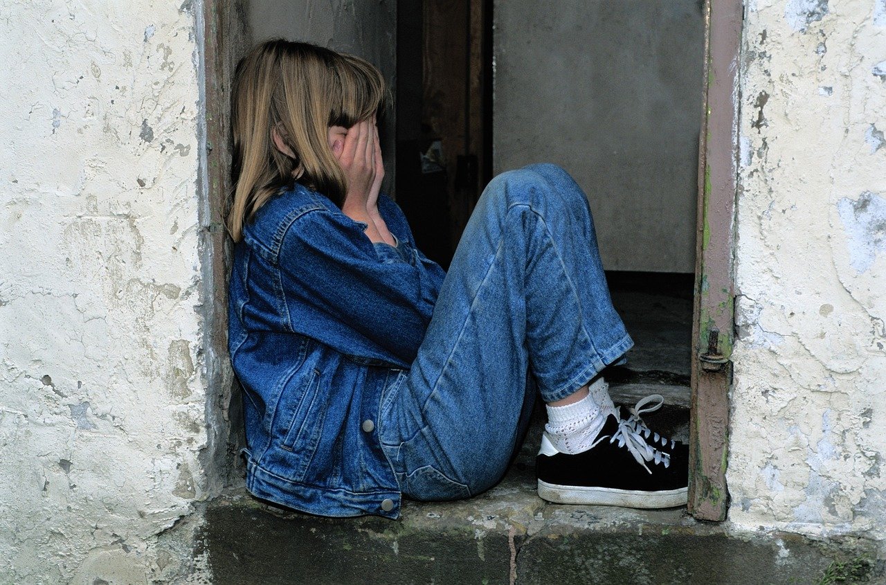 Underwater Model 11 Young woman sitting in an alley covering her face, symbolizing the emotional struggle to overcome imposter syndrome.