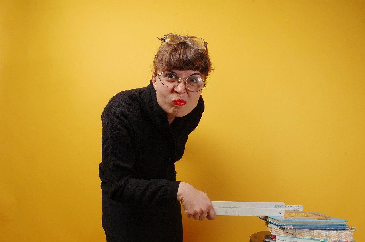 A determined woman with a fierce expression holds a ruler over an open book, embodying a “do your homework” attitude—representing the discipline and focus required to build a successful actor career.