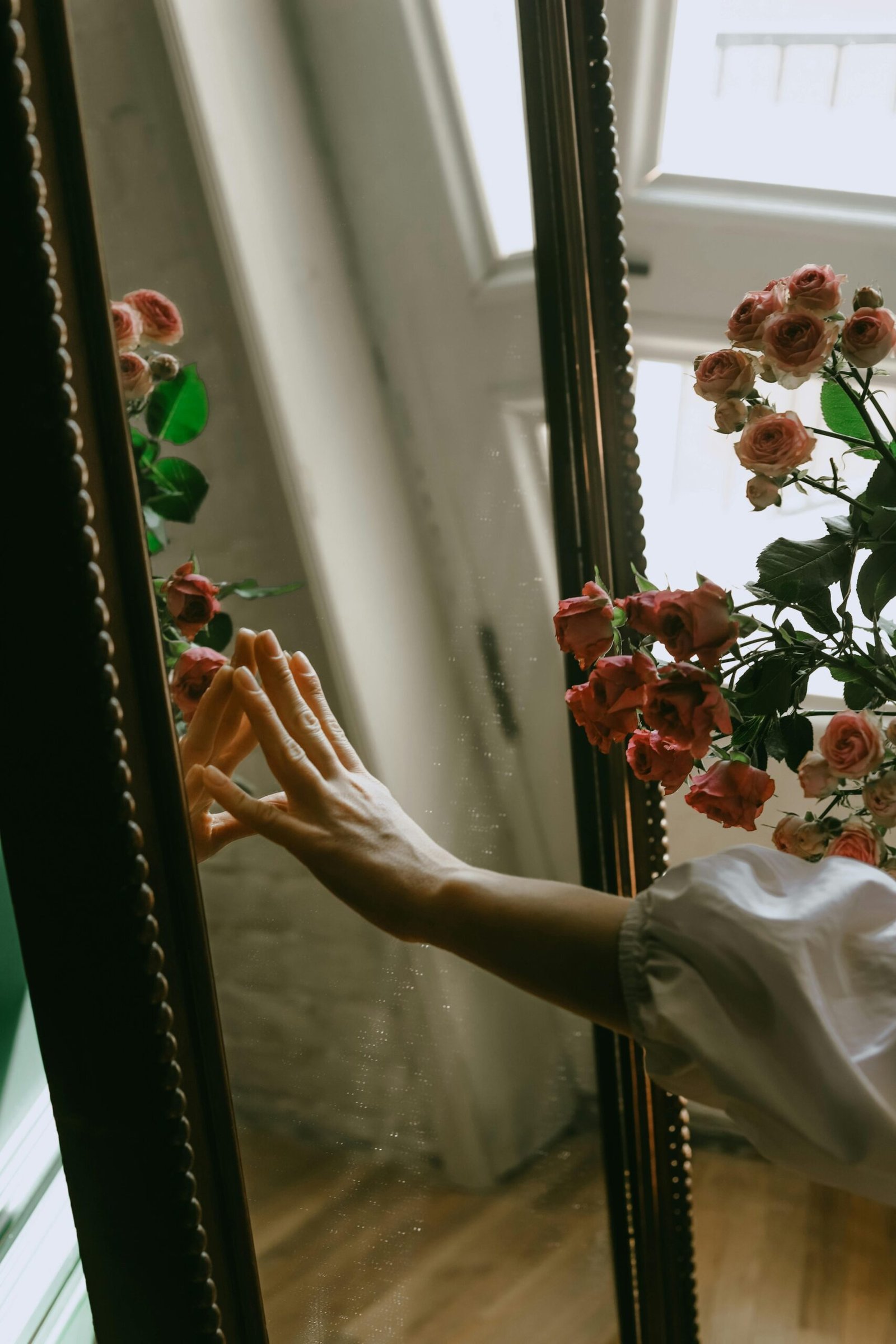 A hand reaching toward a mirror surrounded by delicate flowers, symbolizing introspection and soulful creative services.

