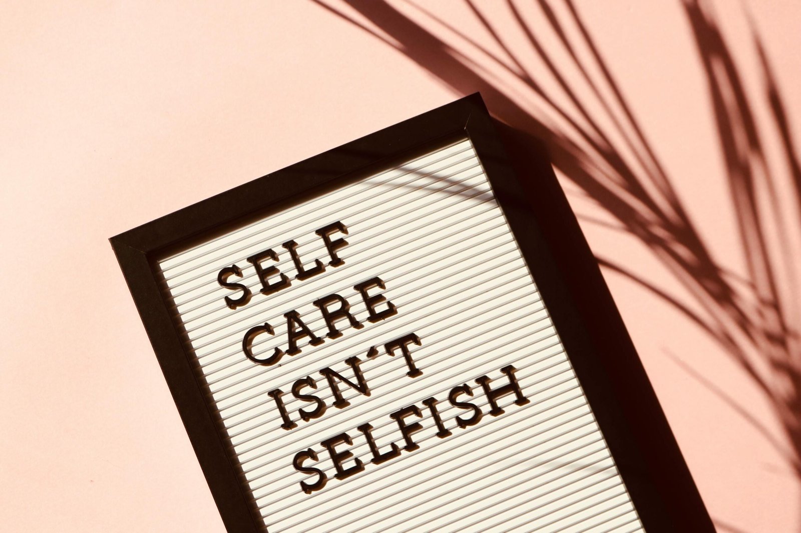 3 Fall Self-Care Rituals for Creatives (and Why We All Need a Little Magic Right Now) 4 Letter board displaying 'Self Care Isn't Selfish' with artistic shadow on pink background - representing mental health for creatives.