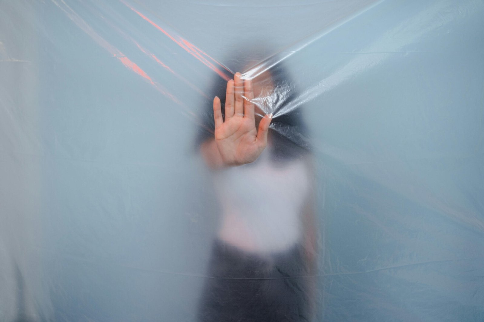 Woman behind a plastic barrier holding her hand up, symbolizing communication boundaries in modeling.