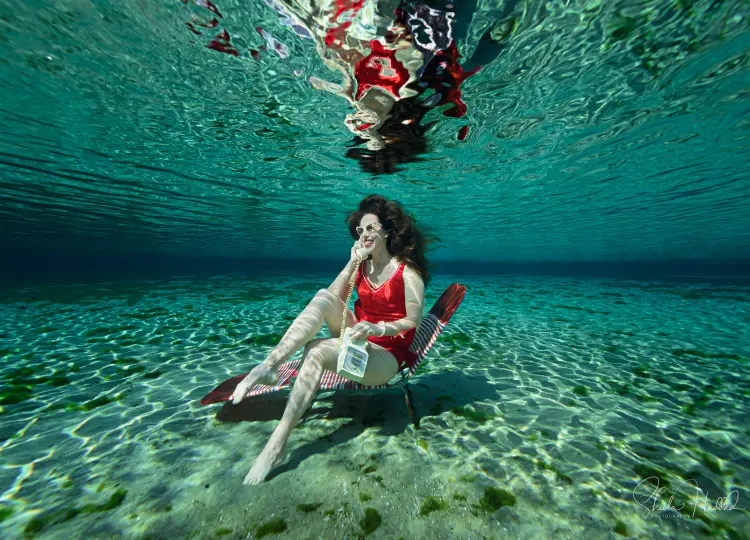 Shannon Scott in a retro red bathing suit taking a call underwater in the Florida Springs.