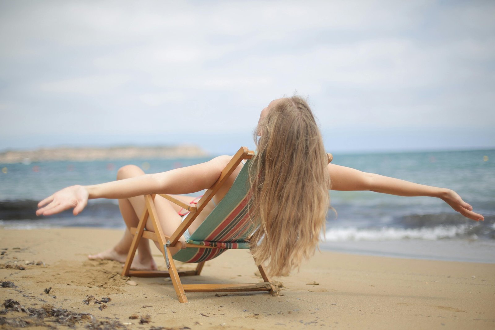 Woman relaxing on a beach chair with arms open wide, representing letting go and calm