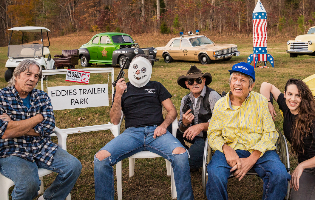 Eddie’s Trailer Park cast posing with cars and the rocket prop behind them during filming.