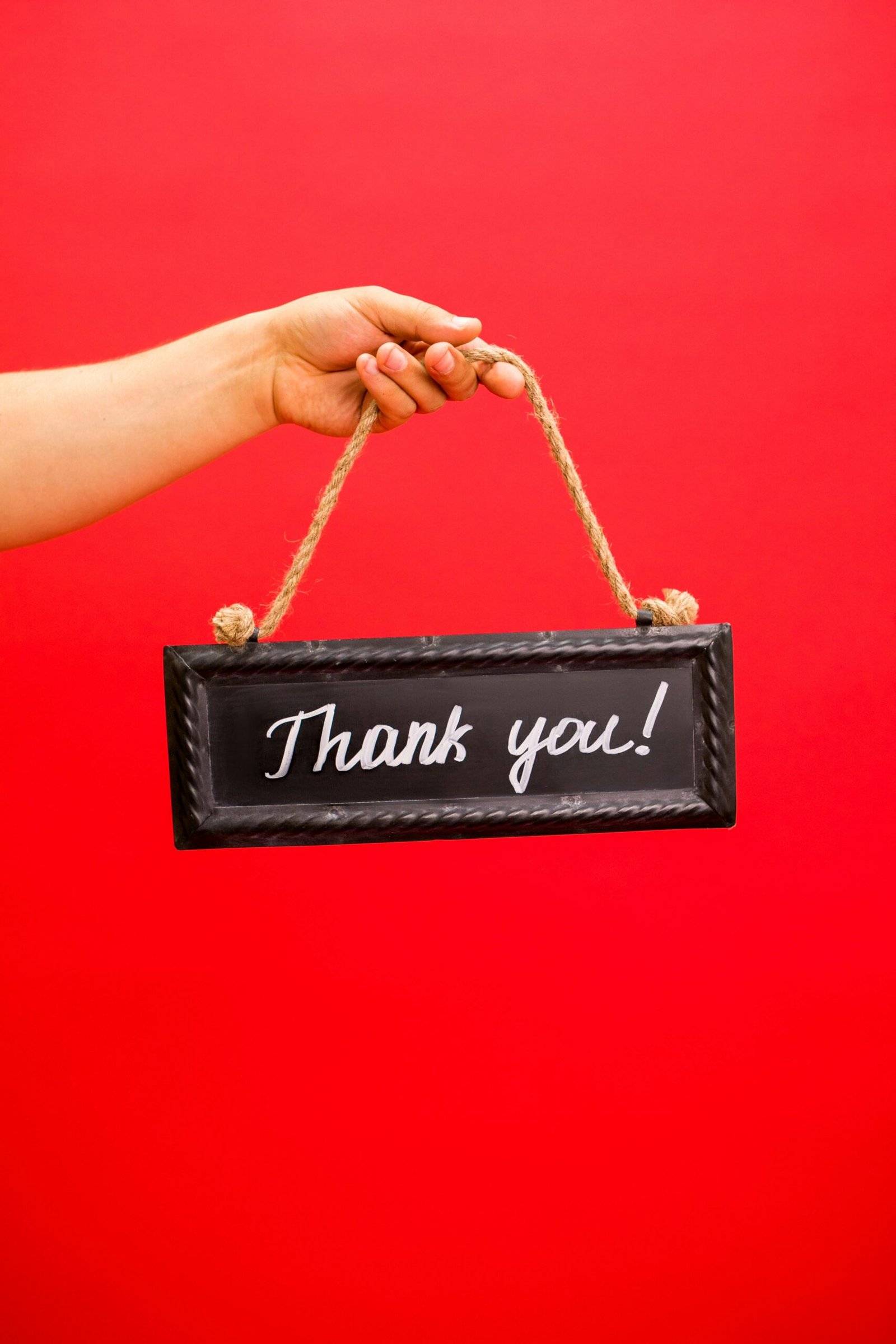 A hand holding a 'Thank You' sign with a red backdrop, perfect for expressions of gratitude.