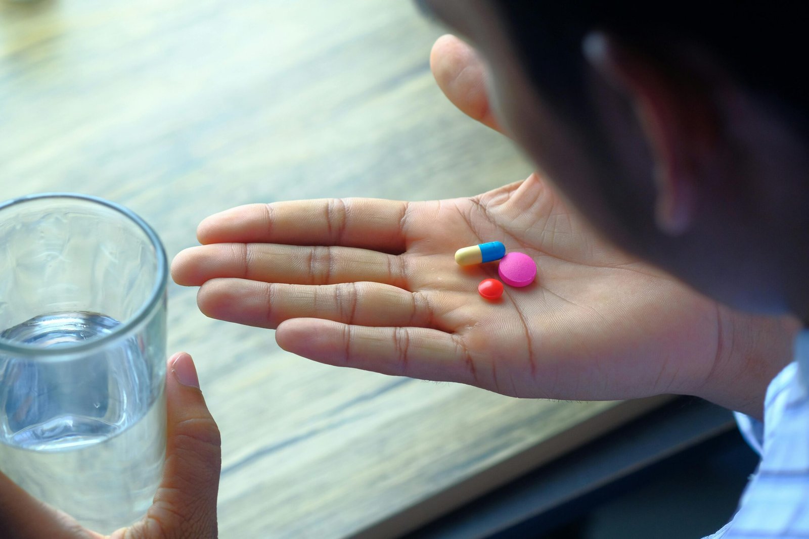 Hand holding prescription pills with a glass of water representing clear medical instructions and patient understanding