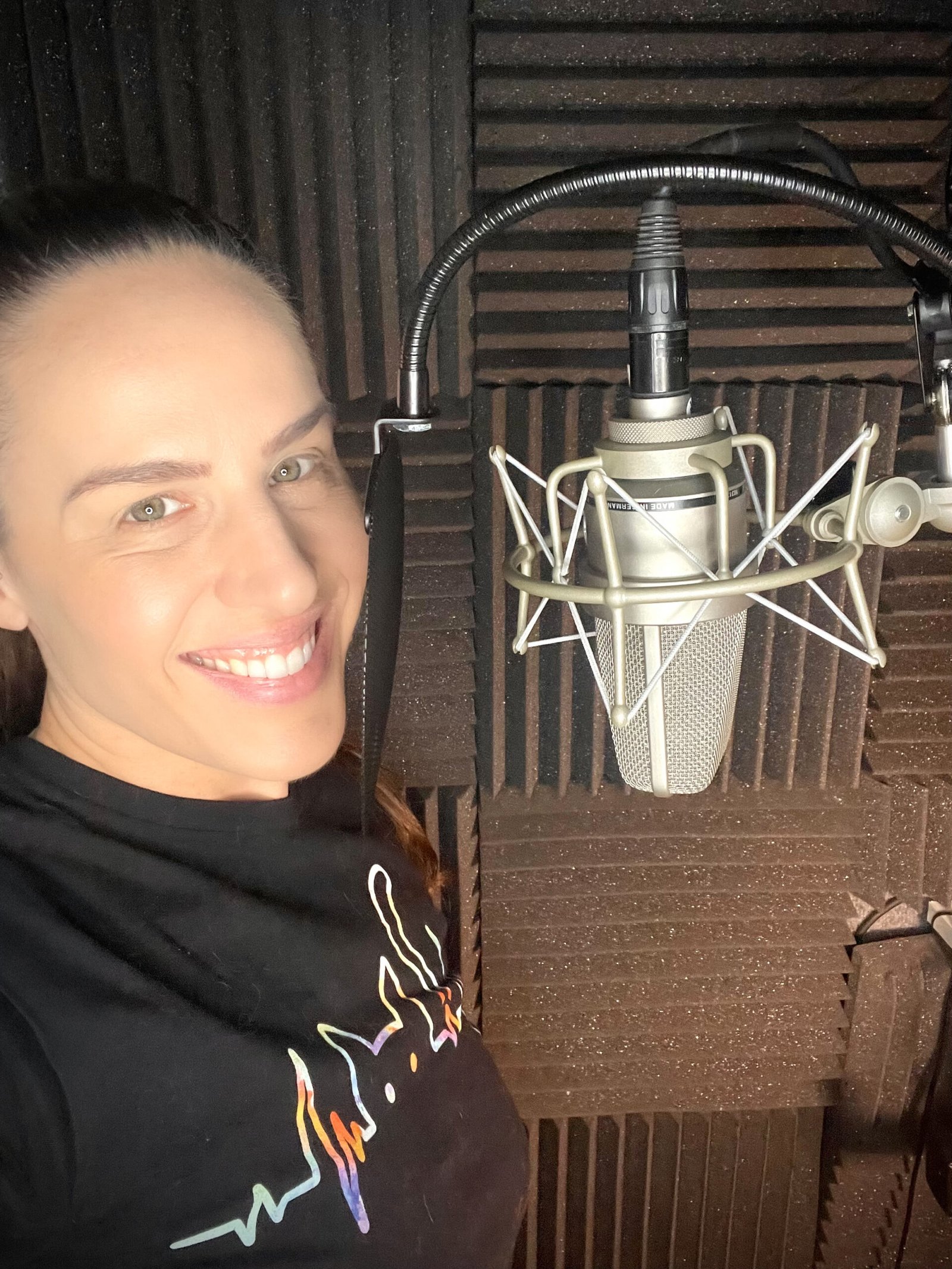 Behind the Scenes in My Professional Voiceover Studio: What Happens During a Voiceover Session 1 Shannon Scott smiling in a professional voiceover studio / recording booth with a condenser microphone and acoustic foam panels